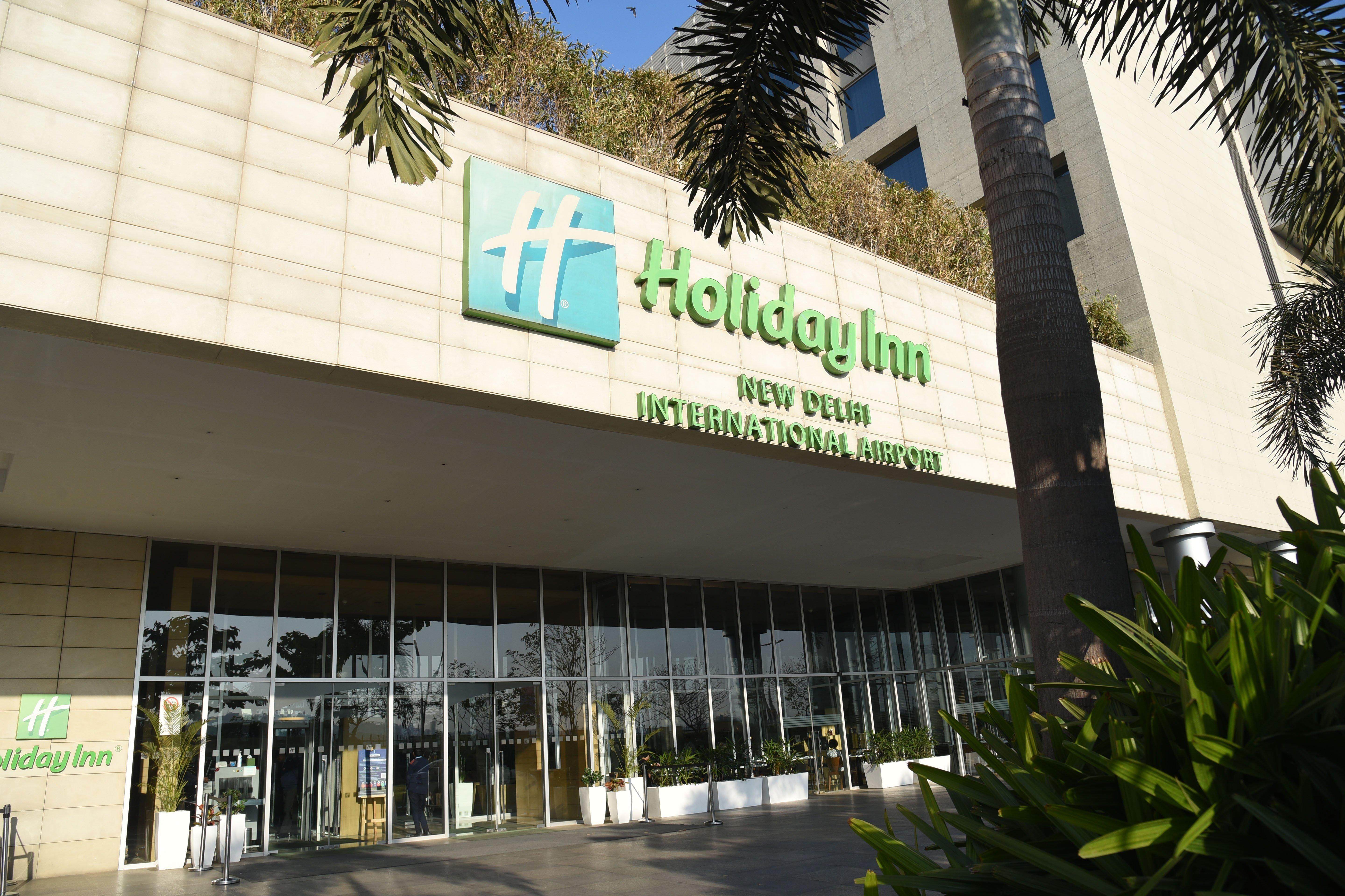 Holiday Inn New Delhi Aerocity By Ihg Ngoại thất bức ảnh The photo shows the exterior of a Holiday Inn hotel, specifically the Holiday Inn New Delhi International Airport. The building features a modern design with a prominent green and white sign displaying the hotel name. There are large glass doors at t